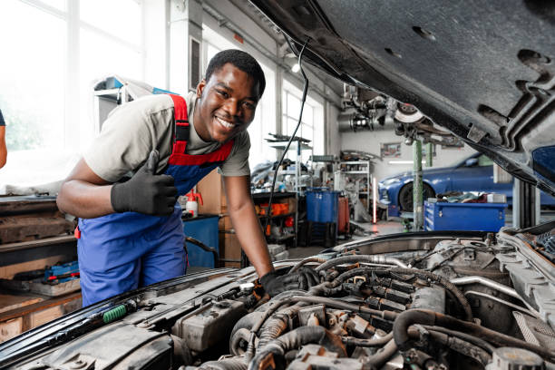 Young African auto mechanic checking car engine under the hood in auto service close up